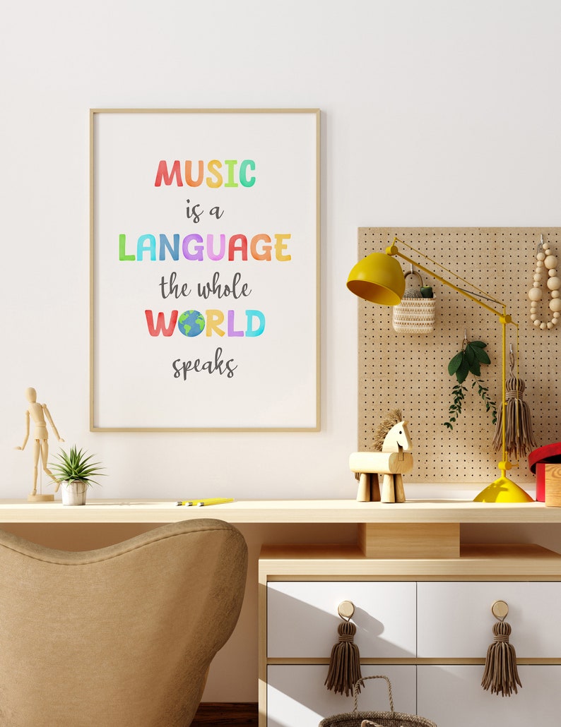 May include: A framed print with the text "MUSIC is a LANGUAGE the whole WORLD speaks" in rainbow colors. The print is hanging on a white wall above a wooden desk with a chair, a lamp, and other decorative items.