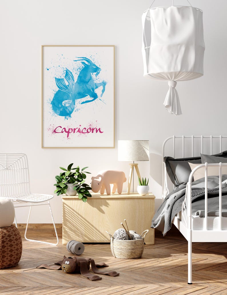 May include: A framed watercolor print featuring the Capricorn zodiac sign in shades of blue and pink. The artwork depicts a goat-fish hybrid with the word "Capricorn" below. The print hangs above a wooden chest with a lamp and decorative items.