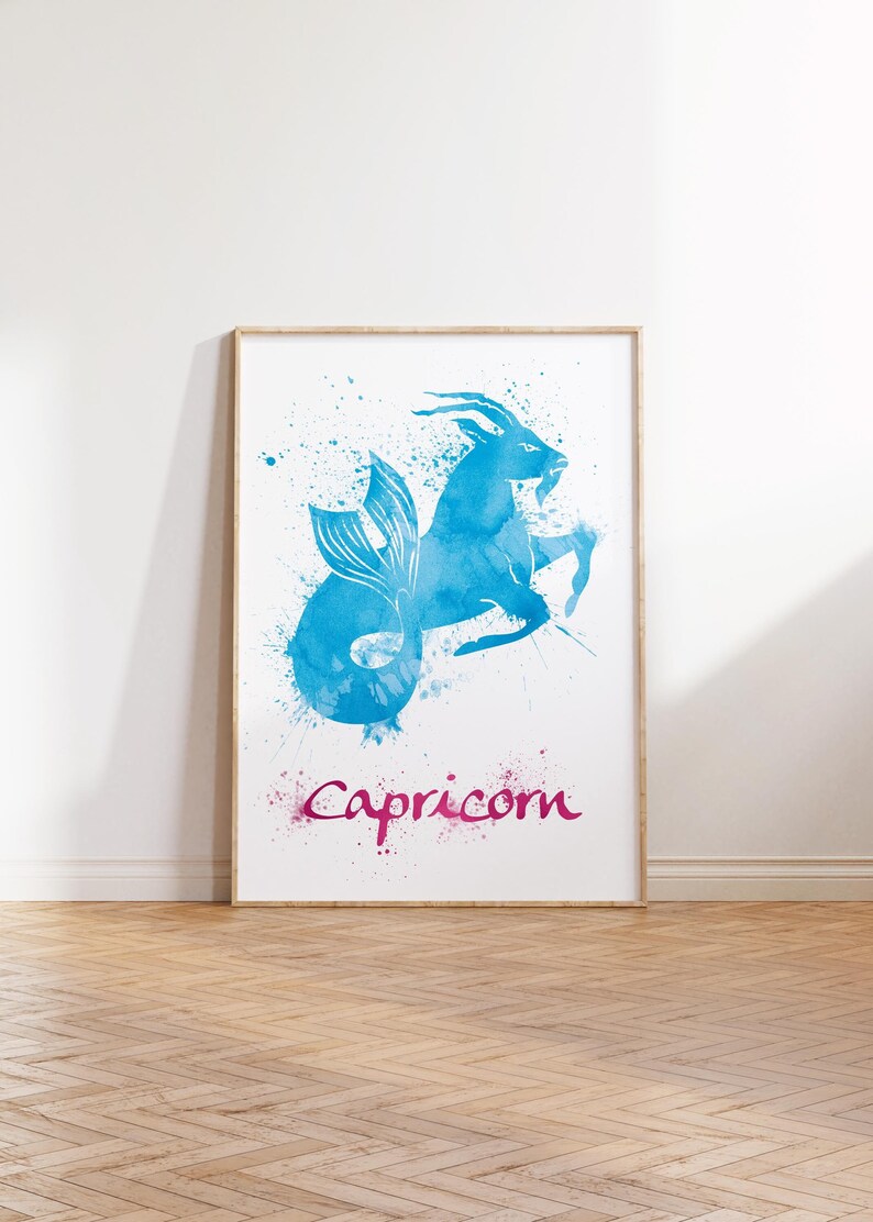 May include: A framed art print featuring a blue watercolor illustration of the Capricorn zodiac sign. The image depicts a goat with a fish tail, with the word "Capricorn" in pink script below. The artwork is displayed on a white background.