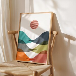 May include: Abstract art print featuring a red sun and colourful waves in shades of teal, blue, green, orange, and red. The print is framed in a natural wood frame.