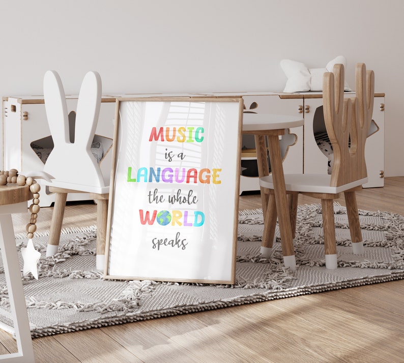 May include: A white framed print with the text "MUSIC is a LANGUAGE the whole WORLD speaks" in rainbow colors. The print is hanging on a white wall in a room with a white rug and two wooden chairs.