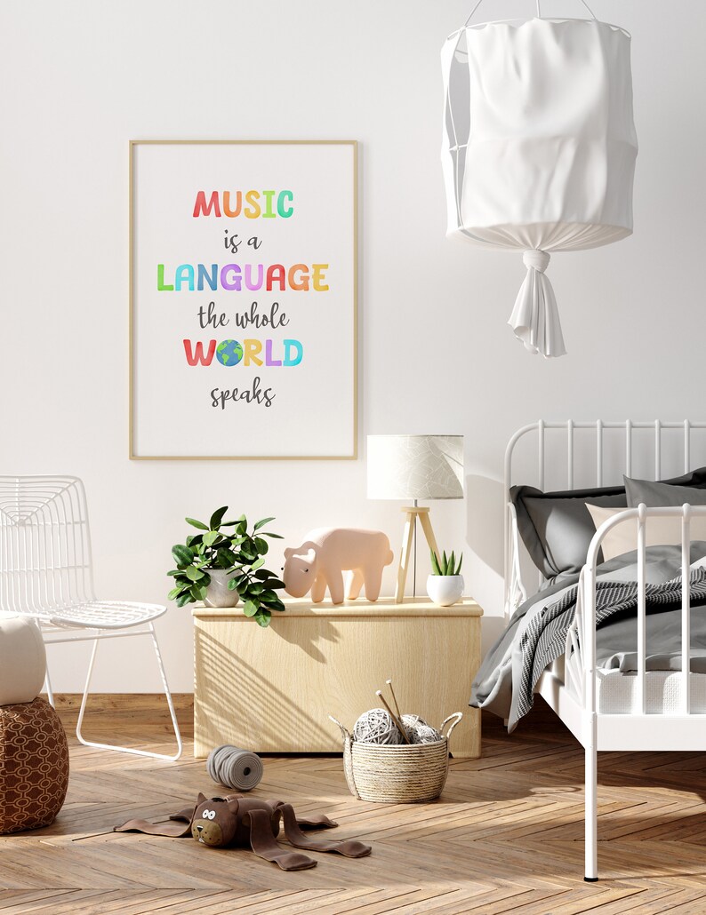 May include: A framed print with the text "MUSIC is a LANGUAGE the whole WORLD speaks" in a rainbow of colors. The print is hanging on a white wall in a room with a white bed, a white chair, and a wooden side table.