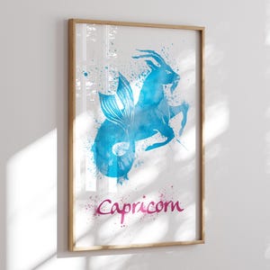 May include: Framed watercolor print featuring the Capricorn zodiac sign. The artwork depicts a blue mythical creature with a fish tail and goat horns, with the word "Capricorn" in pink script. The print is in a wooden frame.