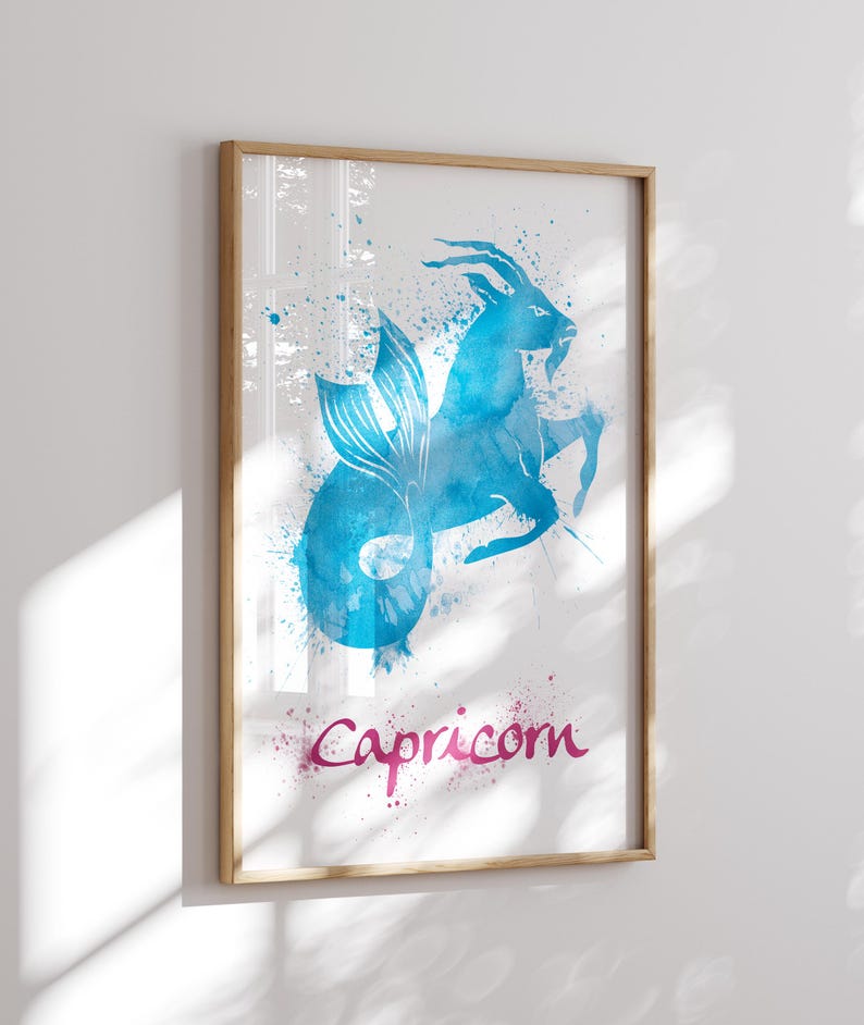 May include: Framed watercolor print featuring the Capricorn zodiac sign. The artwork depicts a blue mythical creature with a fish tail and goat horns, with the word "Capricorn" in pink script. The print is in a wooden frame.