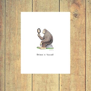 May include: A black and white illustration of a monkey looking at its reflection in a hand mirror. The monkey is sitting on a rock and the text "Believe in Yourself" is below the image.