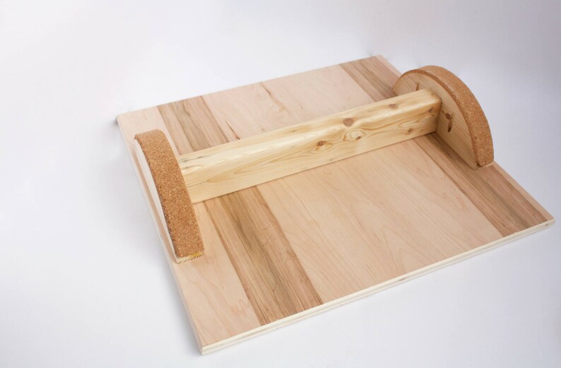 Image of an upside down wooden balance board. The top is made of plywood and is 19 inches square with two strips of grip tape. The rockers are made of reclaimed pine with cork on the bottom to reduce the risk of the board slipping on wood floors.
