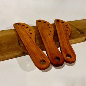 This image includes three herb strippers handmade from reclaimed maple. They are on a piece of an old table from which these herb strippers were made. 

Herbs can be pulled through the incrementally larger holes to separate stems from the leaves.