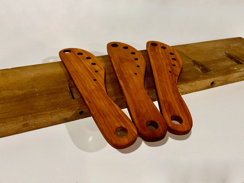 This image includes three herb strippers handmade from reclaimed maple. They are on a piece of an old table from which these herb strippers were made. 

Herbs can be pulled through the incrementally larger holes to separate stems from the leaves.