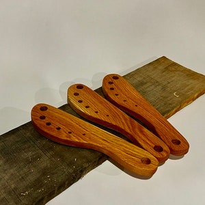 This image includes three herb strippers handmade from reclaimed teak. They are on a piece of a broken pallet from which these herb strippers were made. 

Herbs can be pulled through the incrementally larger holes to separate stems from the leaves.