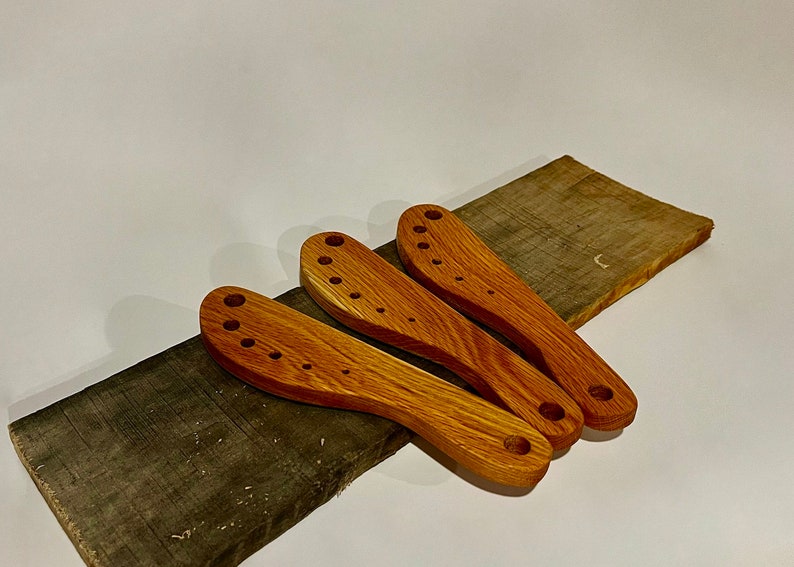 This image includes three herb strippers handmade from reclaimed teak. They are on a piece of a broken pallet from which these herb strippers were made. 

Herbs can be pulled through the incrementally larger holes to separate stems from the leaves.