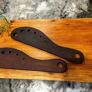 This image includes two handmade herb strippers made from walnut. 

These herb strippers include incrementally larger holes that a cook can use to pull herbs through to separate the stems from the leaves.