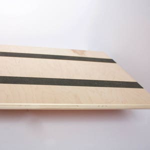 Image of the top of a wooden balance board. The top is made of plywood and is 19 inches square with two strips of grip tape. The rockers are made of reclaimed pine with cork on the bottom to reduce the risk of the board slipping on wood floors.