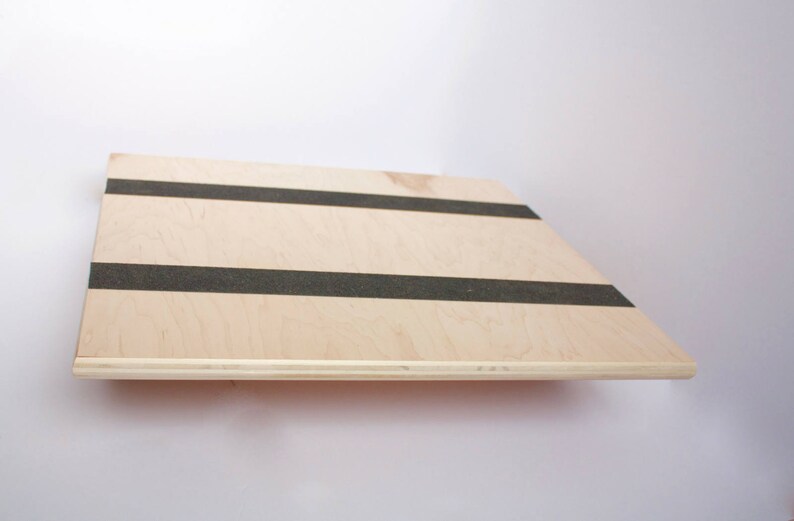 Image of the top of a wooden balance board. The top is made of plywood and is 19 inches square with two strips of grip tape. The rockers are made of reclaimed pine with cork on the bottom to reduce the risk of the board slipping on wood floors.