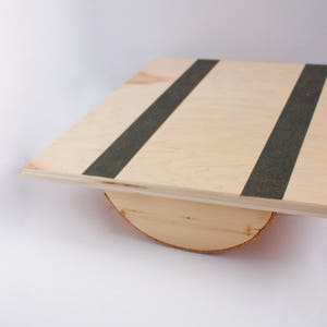 Image of a wooden balance board. The top is made of plywood and is 19 inches square with two strips of grip tape. The rockers are made of reclaimed pine with cork on the bottom to reduce the risk of the board slipping on wood floors.