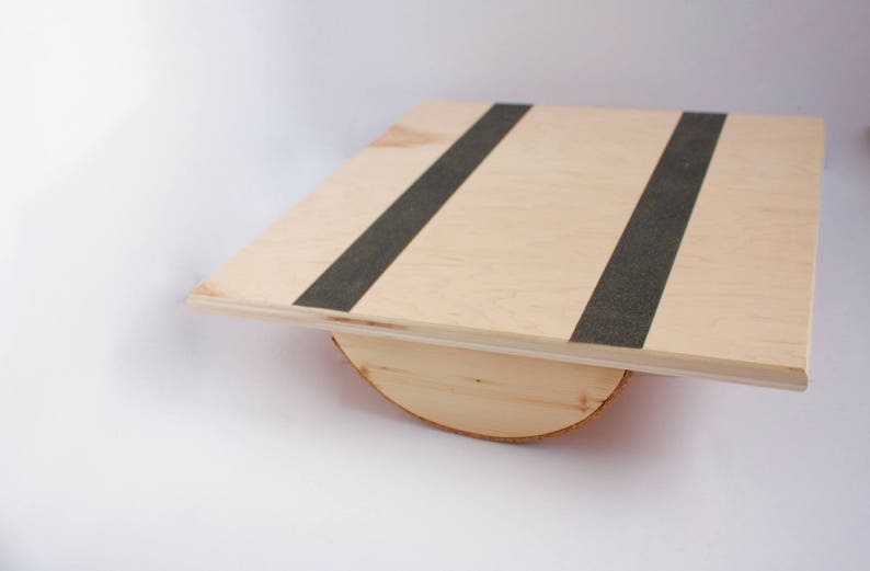 Image of a wooden balance board. The top is made of plywood and is 19 inches square with two strips of grip tape. The rockers are made of reclaimed pine with cork on the bottom to reduce the risk of the board slipping on wood floors.