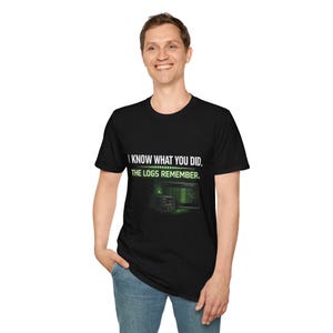 May include: Black t-shirt with the text "I KNOW WHAT YOU DID. THE LOGS REMEMBER." in white and green. The graphic includes a server and a computer screen with green text. The person is wearing blue jeans.