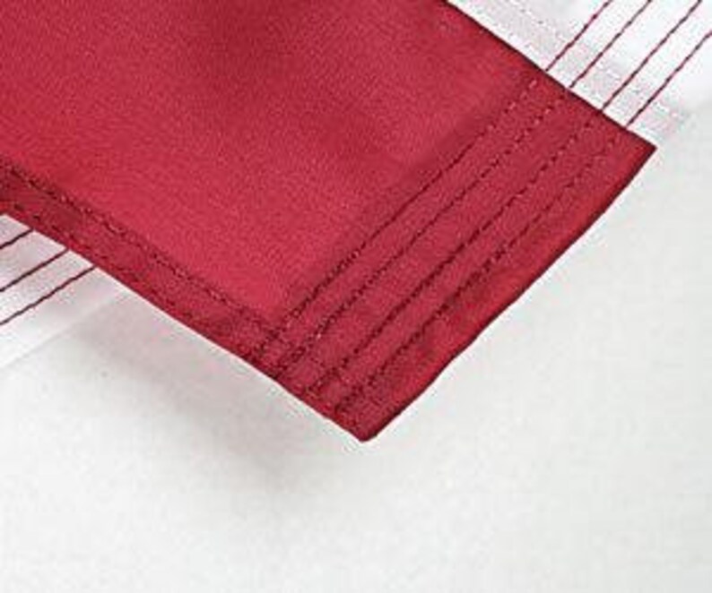 May include: Close-up of the hem of a burgundy garment with multiple rows of stitching.