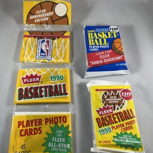 Puede incluir: Varios paquetes sin abrir de cartas de baloncesto Fleer. Los paquetes son amarillos, azules y blancos, con gráficos de baloncesto y texto como "Basketball", "Player Photo Cards" y "Rookie Sensations". Algunos paquetes están marcados con "Fifth Anniversary Edition".
