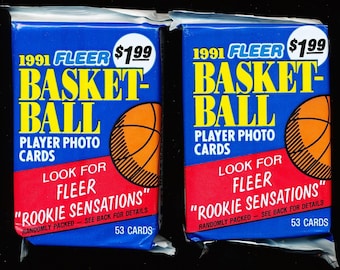 May include: Two sealed packs of 1991 Fleer basketball player photo cards. Each blue wrapper features yellow text reading 1991 FLEER BASKETBALL, a graphic of an orange basketball, and a red banner stating LOOK FOR FLEER ROOKIE SENSATIONS.