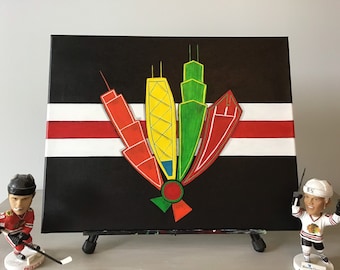 May include: A black canvas painting with a red, white and black striped background. The painting depicts a stylised image of the Chicago skyline in red, yellow, green and blue. The painting is on an easel and there are two hockey player figurines in front of it.