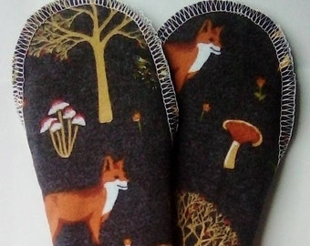 Könnte beinhalten: Zwei dunkelgraue Stoff-Topflappen mit einem weißen Zickzack-Stich an den Rändern. Der Stoff hat ein sich wiederholendes Muster aus orangefarbenen Füchsen, gelben Bäumen und braunen Pilzen.
