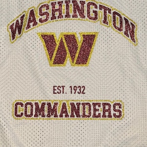 May include: White mesh jersey featuring the word "WASHINGTON" in maroon glitter with gold trim. A maroon glitter "W" with gold trim is centered below. The text "EST. 1932" and "COMMANDERS" are displayed below.