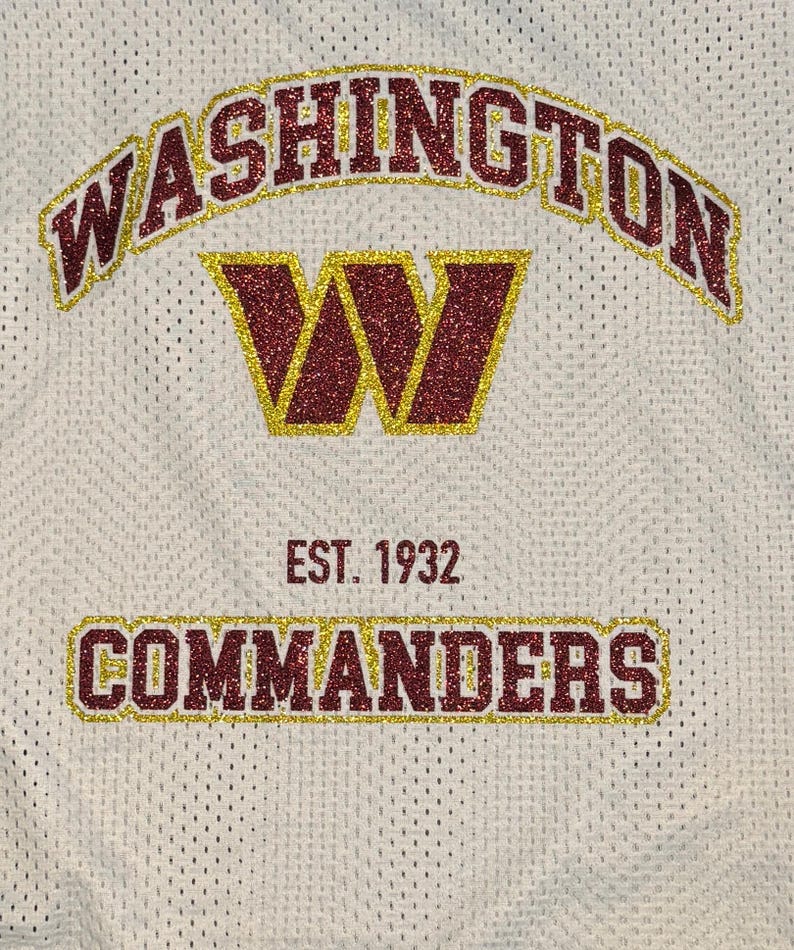 May include: White mesh jersey featuring the word "WASHINGTON" in maroon glitter with gold trim. A maroon glitter "W" with gold trim is centered below. The text "EST. 1932" and "COMMANDERS" are displayed below.