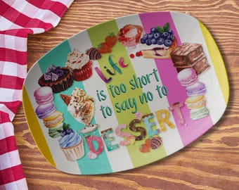 May include: An oval serving platter with a striped design and the words "Life is too short to say no to DESSERT." The platter features illustrations of desserts, including cupcakes, macarons, and chocolate cake. The colour scheme includes pink, green, and yellow.