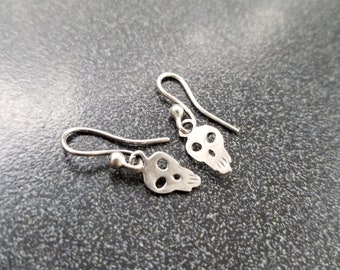 May include: A pair of silver skull earrings with a delicate, openwork design. The earrings are small and lightweight, making them perfect for everyday wear.