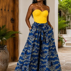 May include: A bright yellow strapless corset top paired with high-waisted, wide-leg trousers featuring a blue, yellow, and white wavy pattern with circular motifs. The trousers include a matching fabric tie belt at the waist and side pockets.