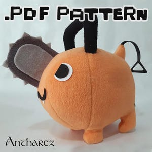 Puede incluir: Un peluche naranja con forma de motosierra con detalles negros. Tiene una hoja de sierra, un mango negro y una pequeña cola. El texto ".PDF PATTERN" está en la parte superior y "Antharez" en la inferior.