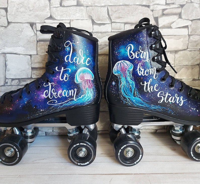 May include: A pair of black roller skates with galaxy-themed designs. One skate features the text "dare to dream" and a jellyfish, while the other skate features the text "Born from the stars" and a jellyfish.