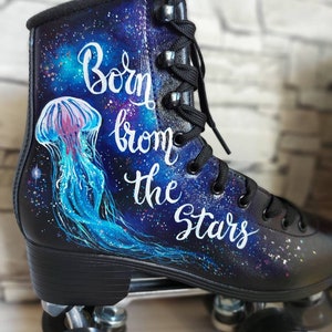 May include: Black roller skates with a galaxy-themed design. The skates feature a blue and purple galaxy with a white jellyfish and the words "Born from the Stars" written in white.