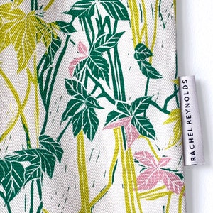 May include: A white fabric tote bag with a green and yellow floral print. The bag has a label on the side that reads "Rachel Reynolds".