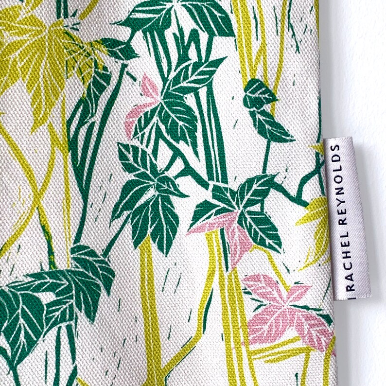 May include: A white fabric tote bag with a green and yellow floral print. The bag has a label on the side that reads "Rachel Reynolds".