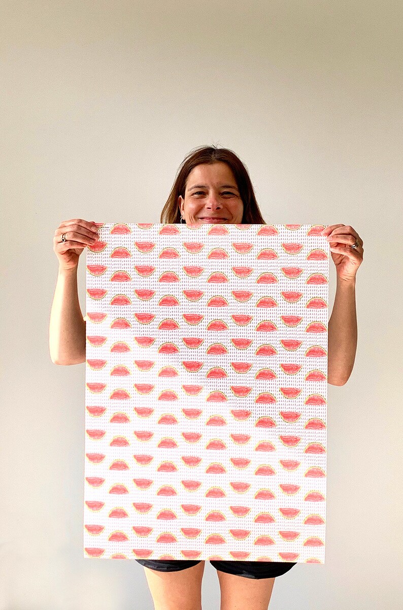 May include: A rectangular white canvas with a repeating pattern of red and yellow watermelon slices. The canvas is held up by a person. The watermelon slices are arranged in rows and columns.