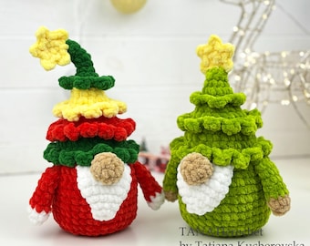 May include: Two handmade Christmas tree gnomes. One is red, yellow, and green with a yellow star on top. The other is green with a yellow star. Both have white beards and tan noses. The gnomes are on a white surface with Christmas lights in the background.