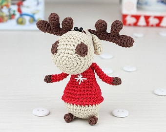 May include: A crocheted reindeer wearing a red sweater with a white snowflake design. The reindeer has brown antlers and brown eyes.