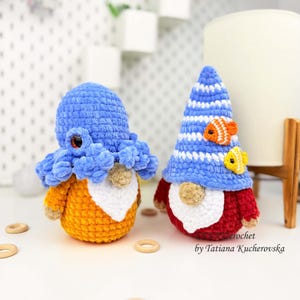 K&ouml;nnte beinhalten: Zwei handgefertigte geh&auml;kelte Zwerge. Einer ist ein Oktopus mit blauem Kopf und orangefarbenem K&ouml;rper. Der andere ist ein Zwerg mit blau-wei&szlig; gestreifter M&uuml;tze, rotem K&ouml;rper und zwei kleinen Fischen. Die Zwerge stehen auf einer wei&szlig;en Oberfl&auml;che.