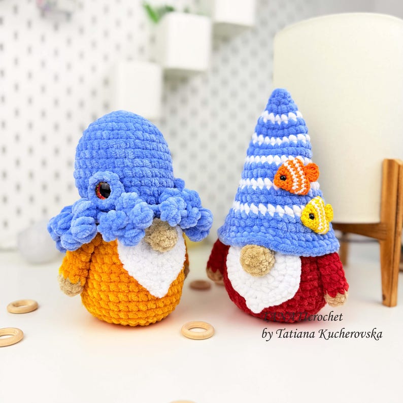 K&ouml;nnte beinhalten: Zwei handgefertigte geh&auml;kelte Zwerge. Einer ist ein Oktopus mit blauem Kopf und orangefarbenem K&ouml;rper. Der andere ist ein Zwerg mit blau-wei&szlig; gestreifter M&uuml;tze, rotem K&ouml;rper und zwei kleinen Fischen. Die Zwerge stehen auf einer wei&szlig;en Oberfl&auml;che.