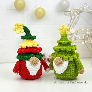 K&ouml;nnte beinhalten: Zwei handgefertigte geh&auml;kelte Weihnachtsbaum-Zwerge. Einer ist rot, gelb und gr&uuml;n mit einem gelben Stern oben. Der andere ist gr&uuml;n mit einem gelben Stern. Beide haben wei&szlig;e B&auml;rte und braune Nasen. Der Text "by Tatiana Kucherovska" ist sichtbar.