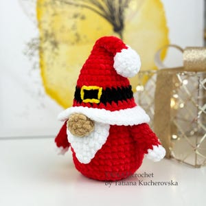 K&ouml;nnte beinhalten: Eine handgefertigte rot-wei&szlig;e H&auml;kelzwerg-Puppe mit Weihnachtsm&uuml;tze, schwarzem G&uuml;rtel und braunem Bart. Der Zwerg hat einen wei&szlig;en Bart und eine goldene Schnalle. Eine festliche Weihnachtsdekoration.