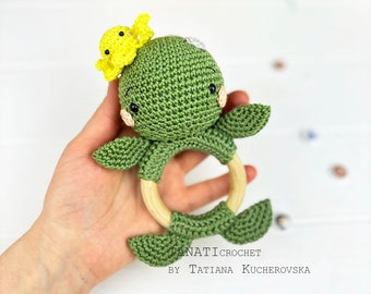 May include: Green crocheted turtle rattle with a yellow crocheted bird on top. The rattle has a wooden ring in the middle.