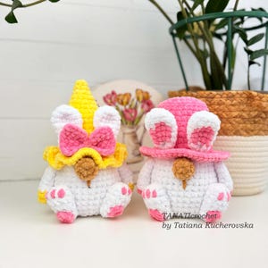 K&ouml;nnte beinhalten: Zwei handgefertigte H&auml;kelzwerge. Einer ist ein Einhorn mit gelbem Horn, rosa Schleife und gelbem Kragen. Der andere ist ein Hase mit rosa Hut und Ohren. Beide sind wei&szlig; mit rosa Akzenten und einer braunen Nase. Der Text "TANATICROCHET by Tatiana Kucherovska" ist sichtbar.