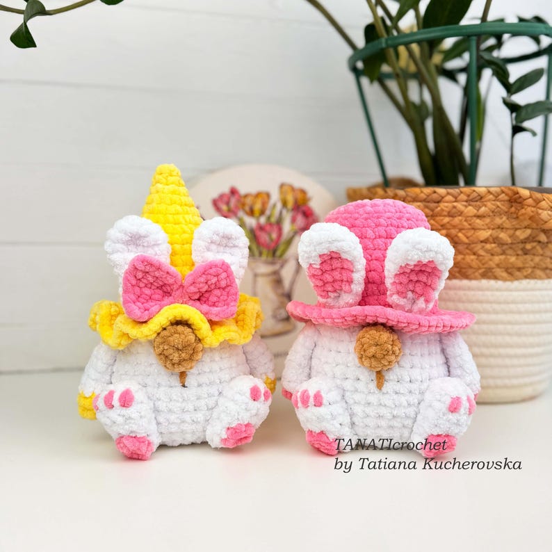 K&ouml;nnte beinhalten: Zwei handgefertigte H&auml;kelzwerge. Einer ist ein Einhorn mit gelbem Horn, rosa Schleife und gelbem Kragen. Der andere ist ein Hase mit rosa Hut und Ohren. Beide sind wei&szlig; mit rosa Akzenten und einer braunen Nase. Der Text "TANATICROCHET by Tatiana Kucherovska" ist sichtbar.