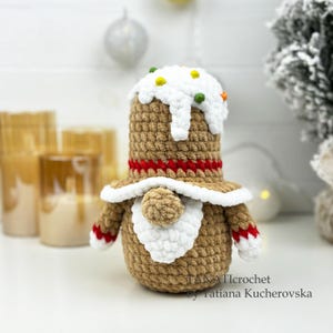 K&ouml;nnte beinhalten: Geh&auml;kelte Lebkuchenmann-Puppe mit wei&szlig;er Zuckerguss-Oberseite und bunten Streuseln. Die Puppe hat einen braunen K&ouml;rper, einen roten Streifen und wei&szlig;e Verzierungen. Arme und F&uuml;&szlig;e haben rot-wei&szlig;e Details. Eine festliche Weihnachtsdekoration.