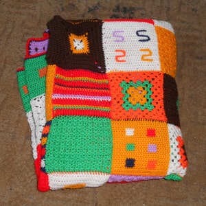 Może przedstawiać: Kolorowy, dziergany na szydełku koc wykonany z kwadrat&oacute;w w r&oacute;żnych kolorach, w tym pomarańczowym, zielonym, czerwonym, białym i brązowym. Kwadraty są zszyte ze sobą, tworząc patchworkowy wz&oacute;r.