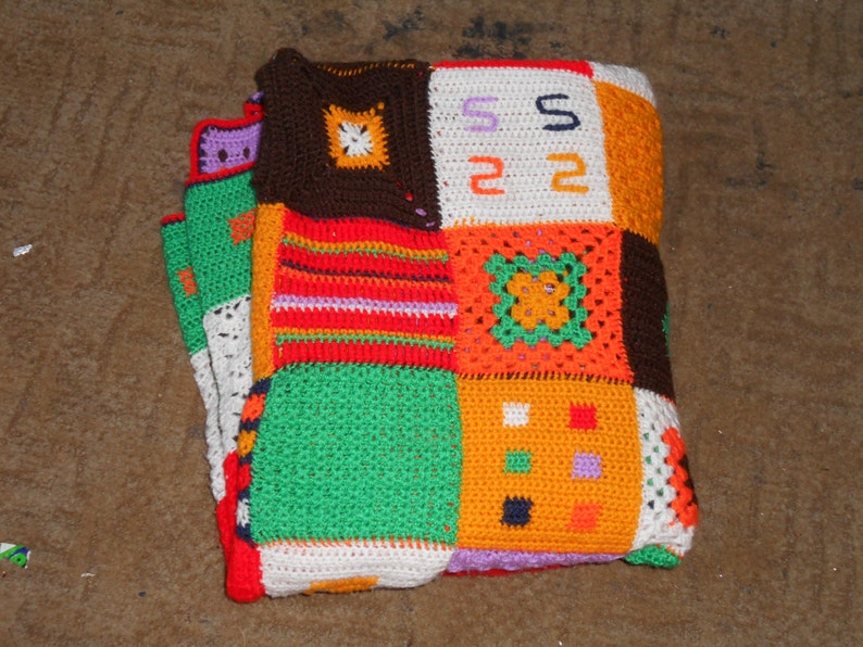 Może przedstawiać: Kolorowy, dziergany na szydełku koc wykonany z kwadrat&oacute;w w r&oacute;żnych kolorach, w tym pomarańczowym, zielonym, czerwonym, białym i brązowym. Kwadraty są zszyte ze sobą, tworząc patchworkowy wz&oacute;r.