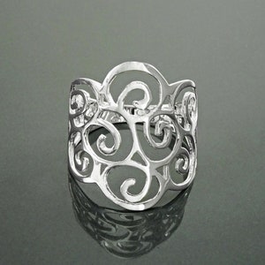Puede incluir: Un anillo de plata con un diseño delicado e intrincado de patrones de espiral calados. El anillo es ancho y tiene una forma redondeada.