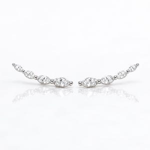 May include: A pair of silver-toned ear climbers featuring a curved design set with four marquise-cut clear stones each. The stones are arranged in a graduated row, creating a sleek, elongated silhouette that follows the natural curve of an earlobe.